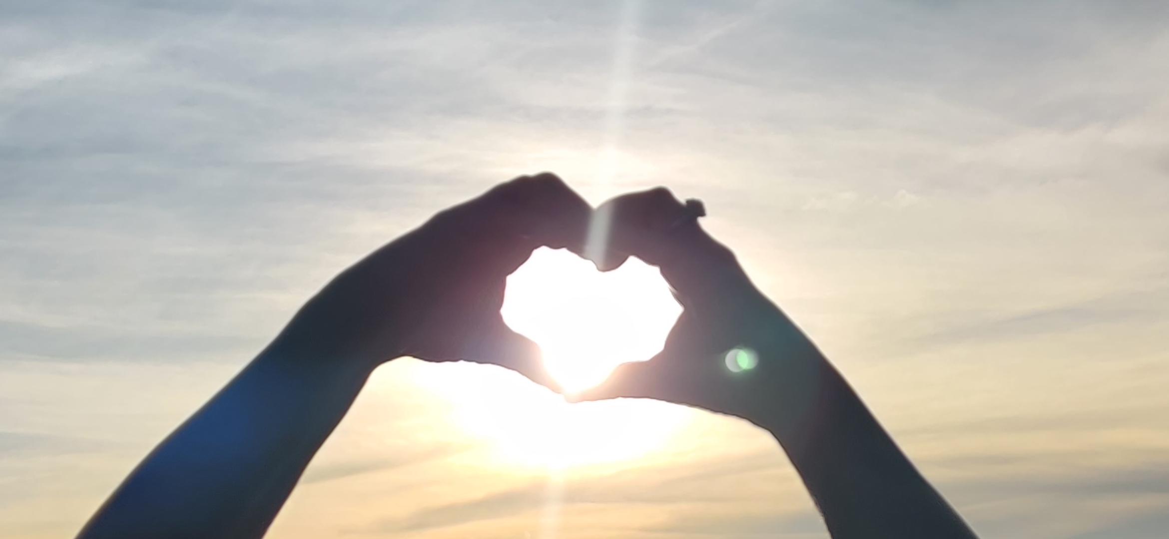 A photo of the sun through hands forming a heart